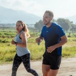 Two adults running on a rural dirt path, enjoying a sunny day outdoors.
